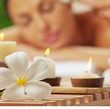 a flower and candles with a woman having a massage in the background